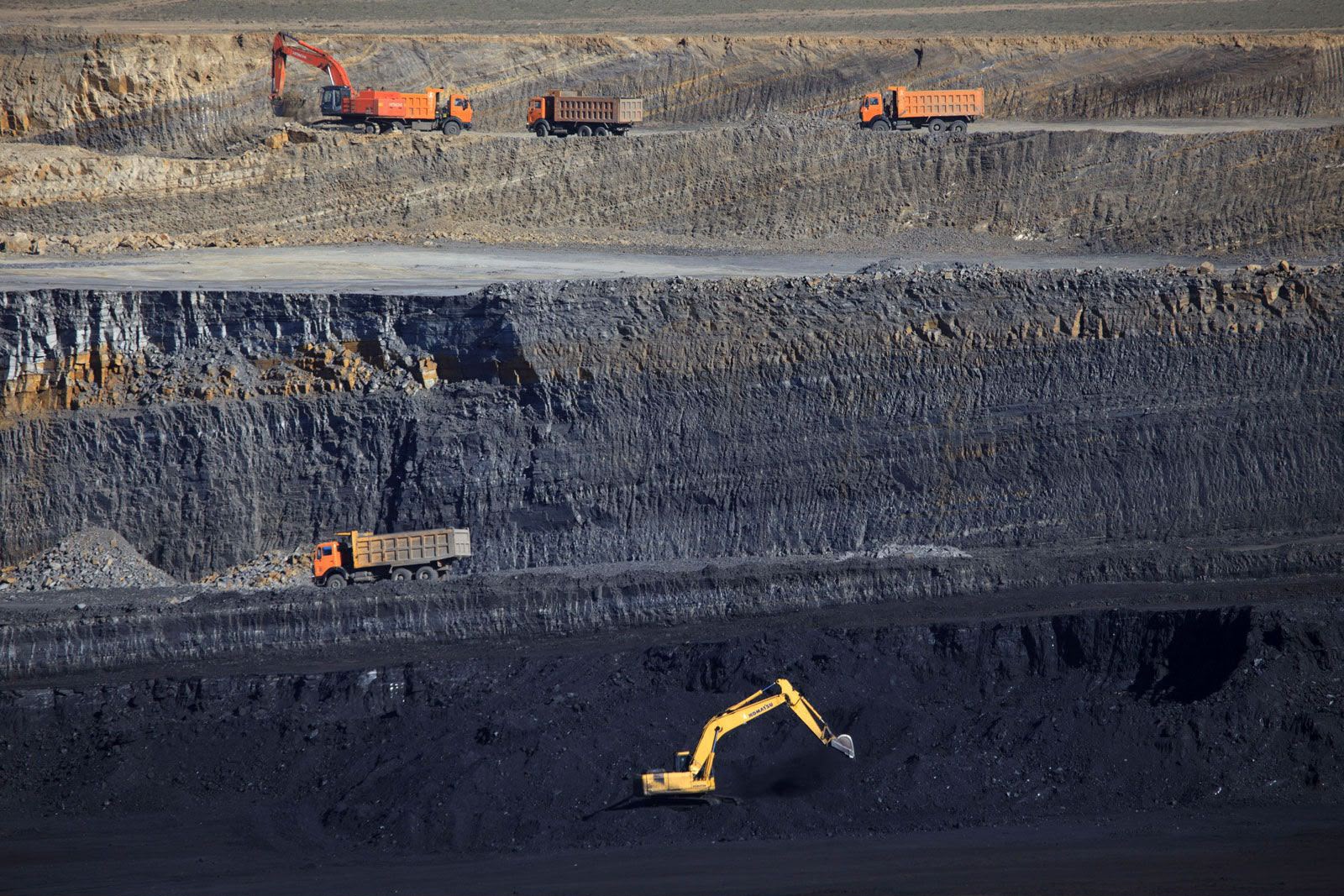 Terraced open-pit coal mine with excavators and haul trucks on the benches